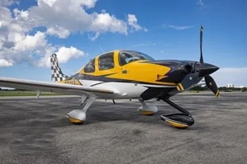 Yellow, black, and white aircraft parked outdoors under a blue sky