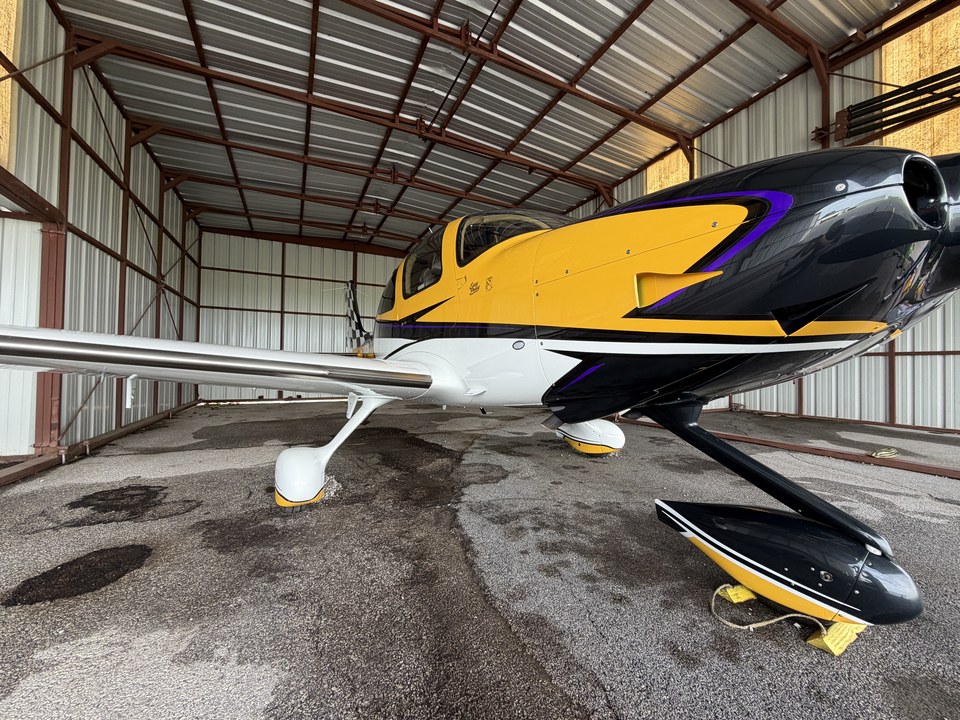 Yellow, black, and white aircraft shown from the side inside a hangar